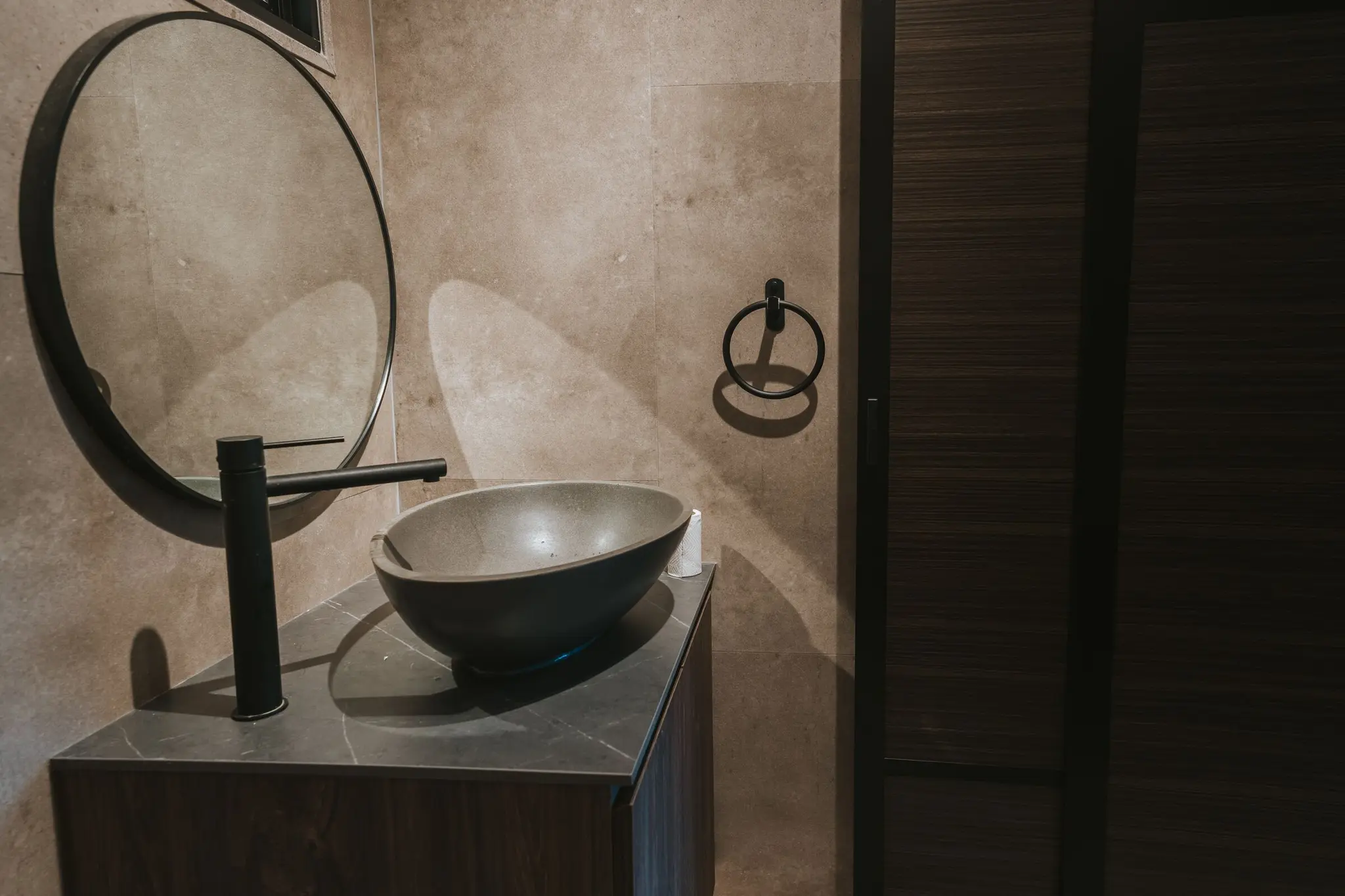 Stone-look bathroom with a round mirror at 213C Punggol Walk