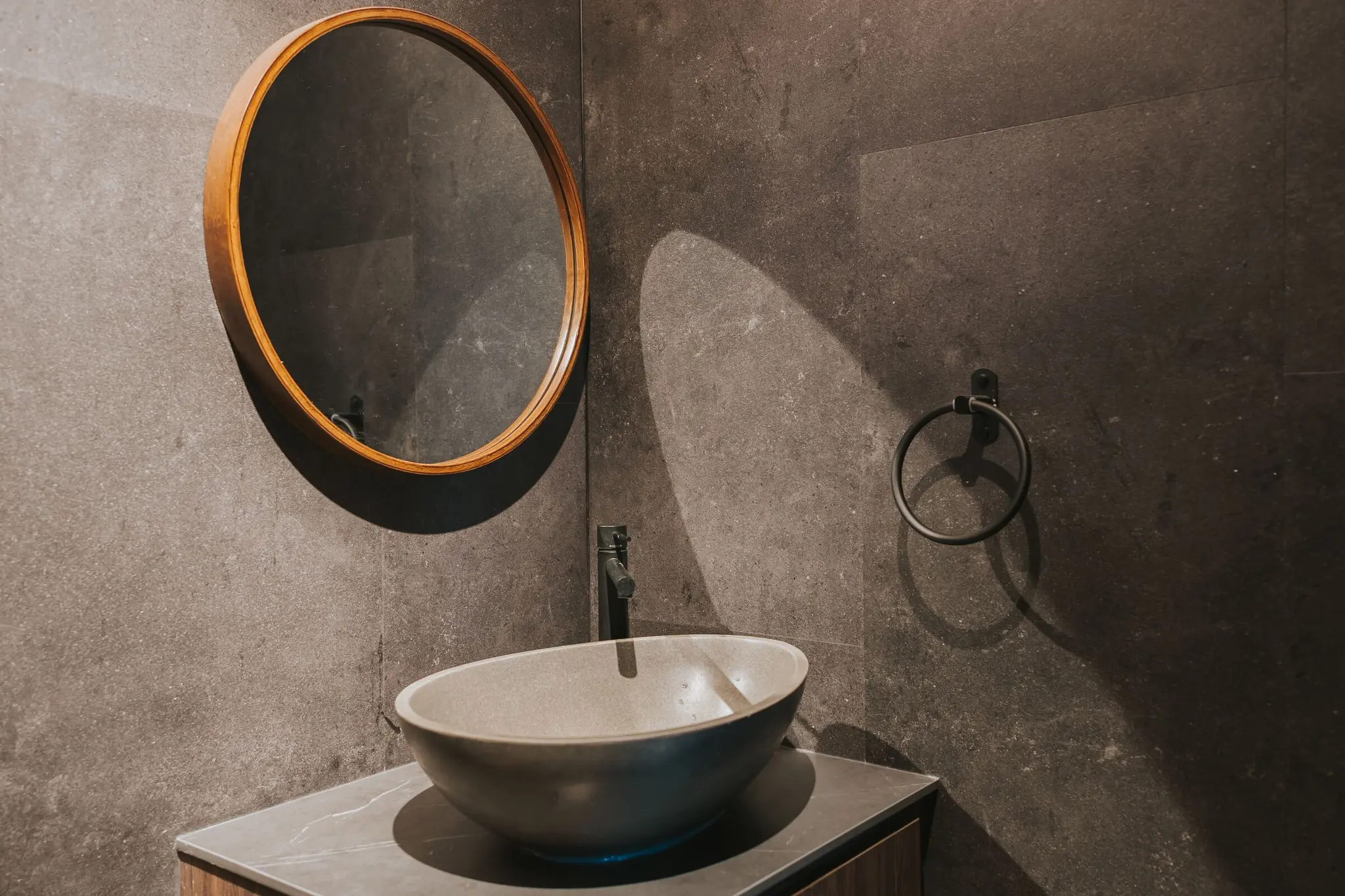 Stone-look bathroom with a round mirror at 213C Punggol Walk